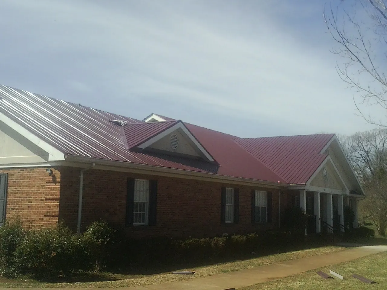 Red metal roof with gabled entries on a long brick building, from a Hail Damage Roof Repair job in Mount Orab
