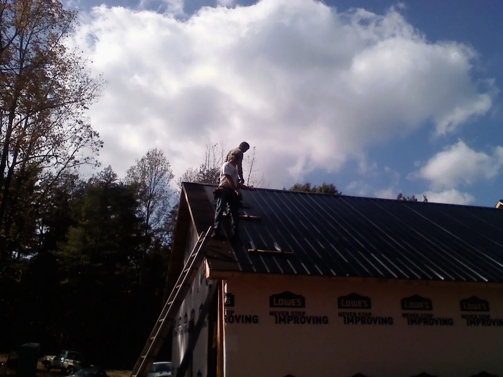 Roofer fastening dark metal panels high against a cloudy sky, from a Roof Inspection job in Mount Orab