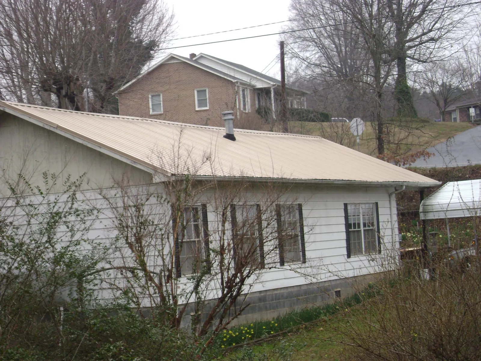 Tan metal roof on a white sided house set into a hillside — Commercial Roofing by Roofing Brothers in Mount Orab